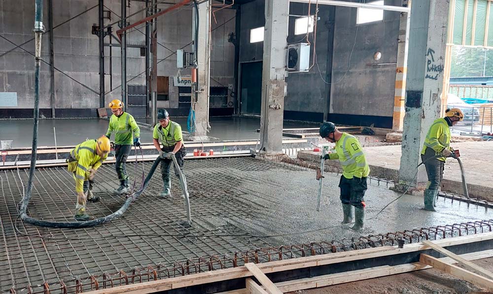 Työntekijöitä työskentelee teollisuushallissa betonilattian valussa.